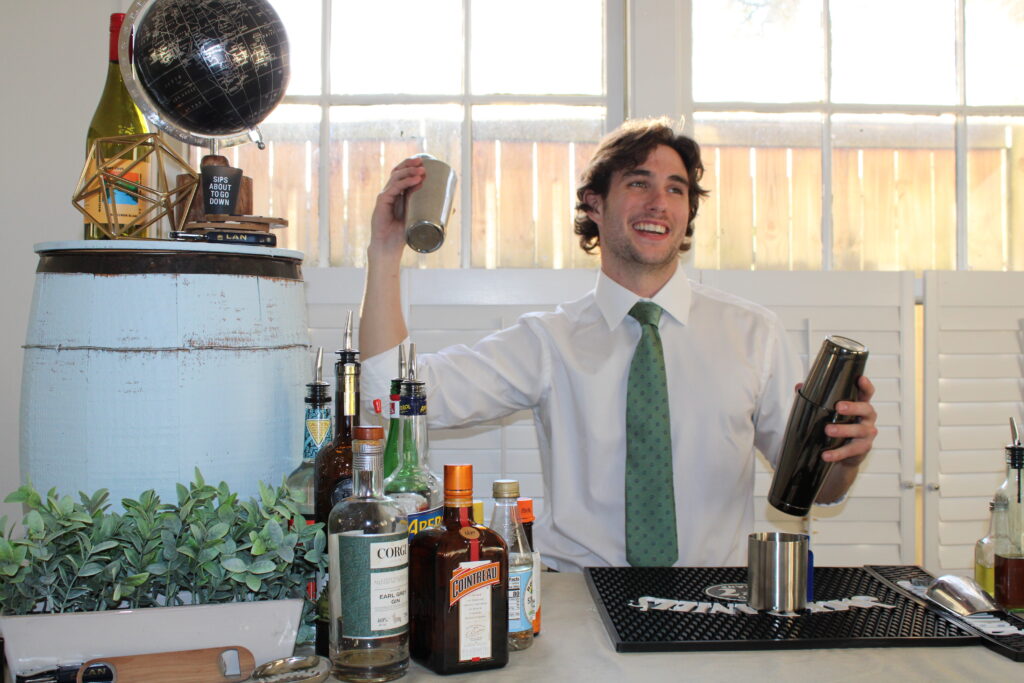 A bartender, using a cocktail shaker in each hand, behind a bar at a wedding. 